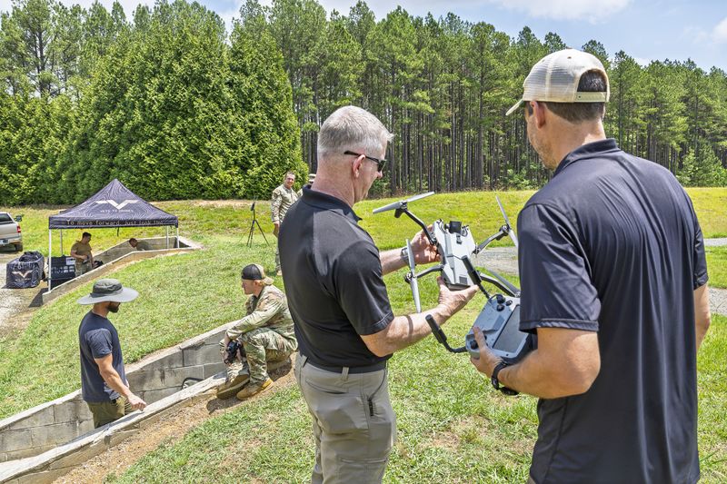 Participants reviewing an uncrewed aircraft and controller during an outdoor field demonstration.